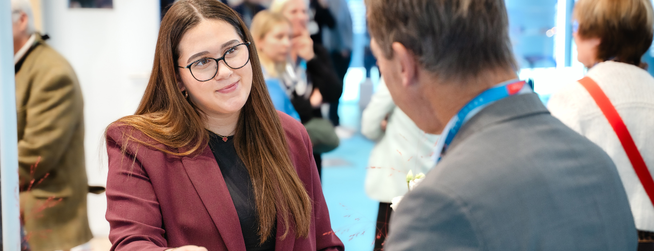 Eine WFB Mitarbeiterin schaut lächelnd einen Besucher von der Veranstaltung an. - Quelle: WFB