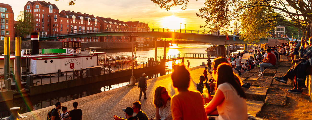 Menschen sitzen im Abendlicht an der Schlachte in Bremen an der Weser. - Quelle: WFB/Jonas Ginter
