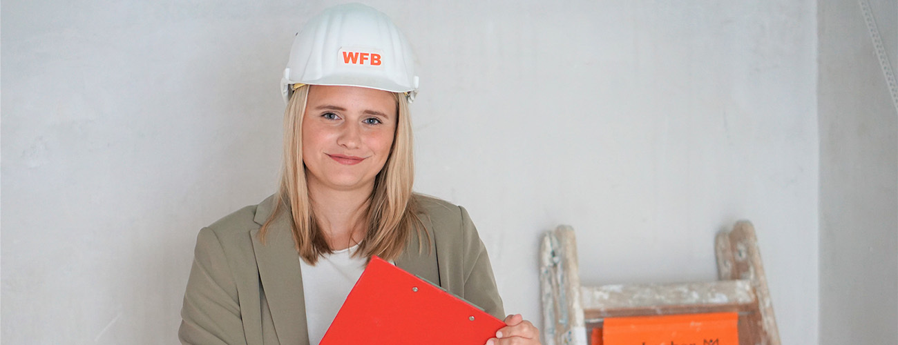 Eine Auszubildende der WFB im Bereich Immobilien und Bau, mit einem Bauhelm auf dem Kopf. - Quelle: WFB