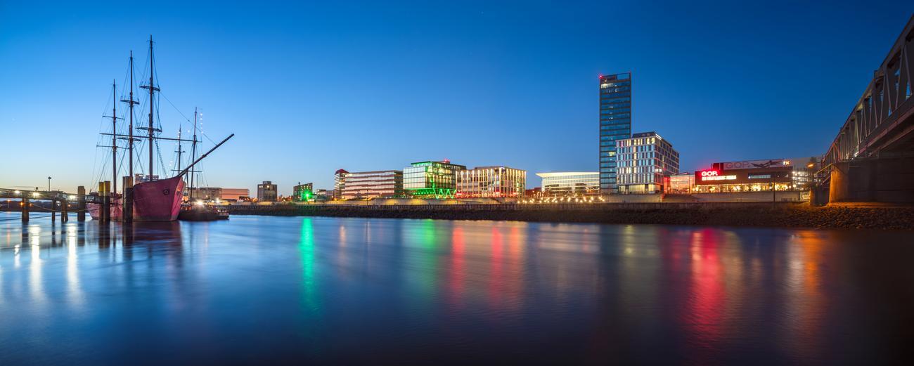 Die Überseestadt im Abendlicht mit Schiff und Weser. - Quelle: WFB/Mario Piera