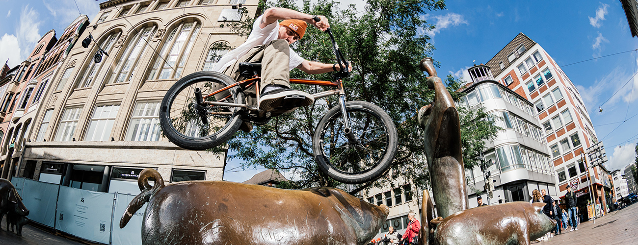 Eine Person springt mit einem BMX-Rad über die Bronzestatue eines Schweins in der Bremer Sögestraße - Quelle: Sportplatz