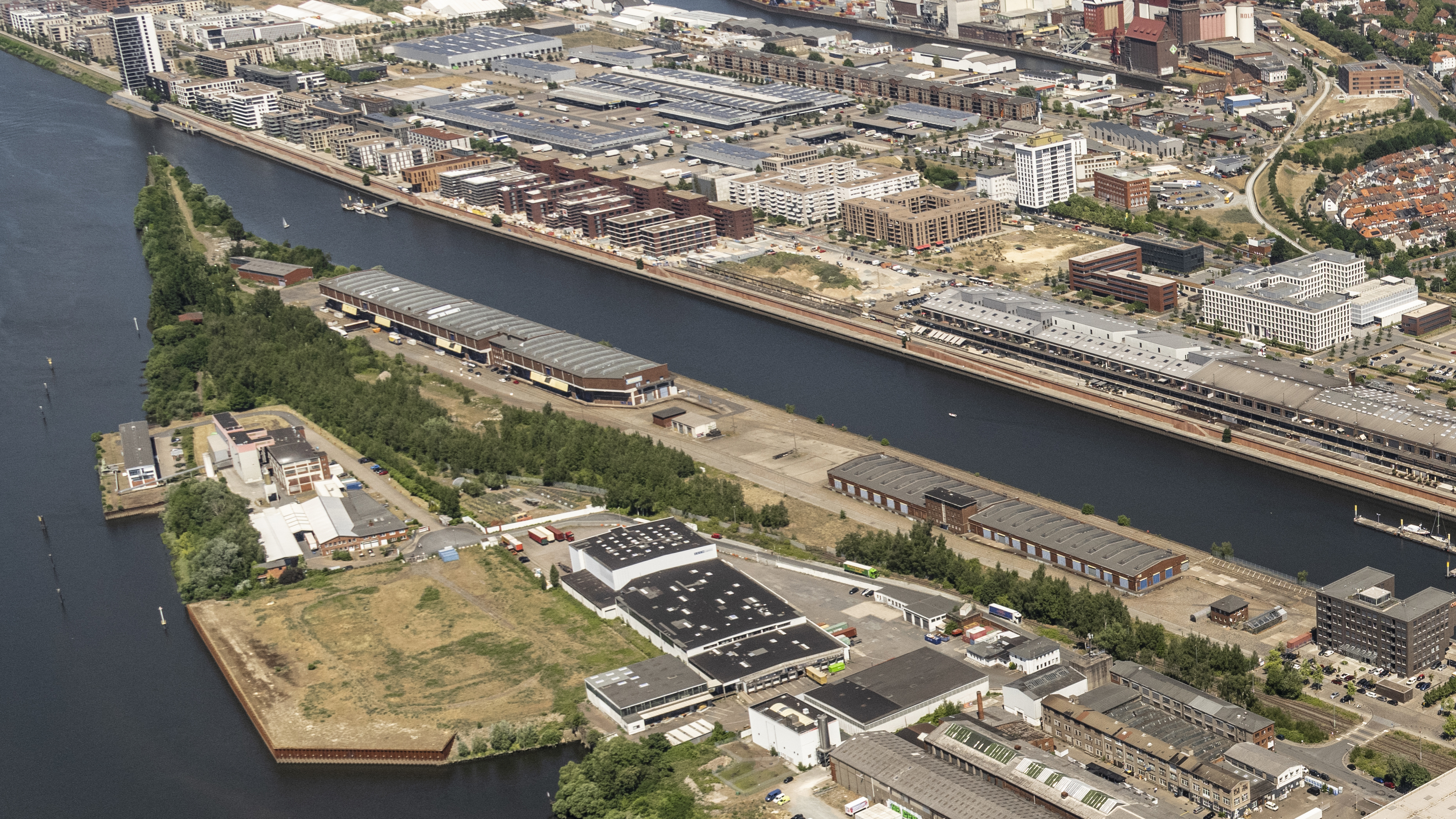 Luftbild einer Landzunge zwischen Europahafen und Weser in der Bremer Überseestadt mit zwei großen Schuppen und weiteren Gebäuden. - Quelle: WFB / Studio B