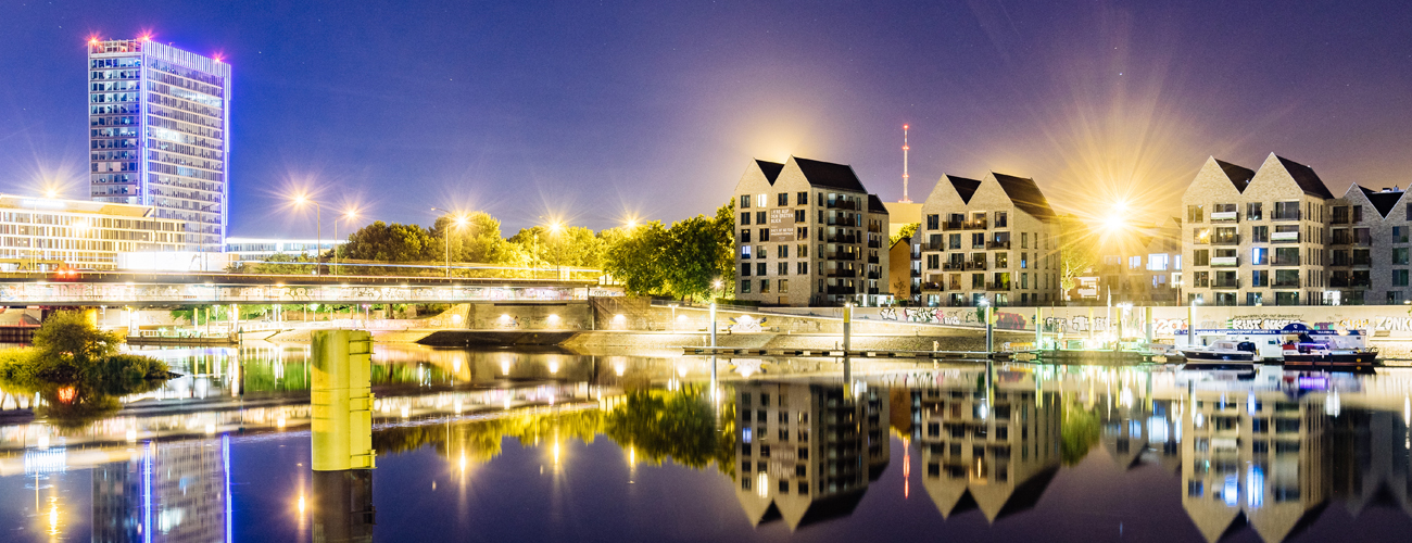 Rechts erkennt man den Weser-Tower, ein Hochhaus mit einer Glasfront, im Vordergrund ist die Weser. Die umliegenden Gebäude und Lichter spiegeln sich im Wasser.
