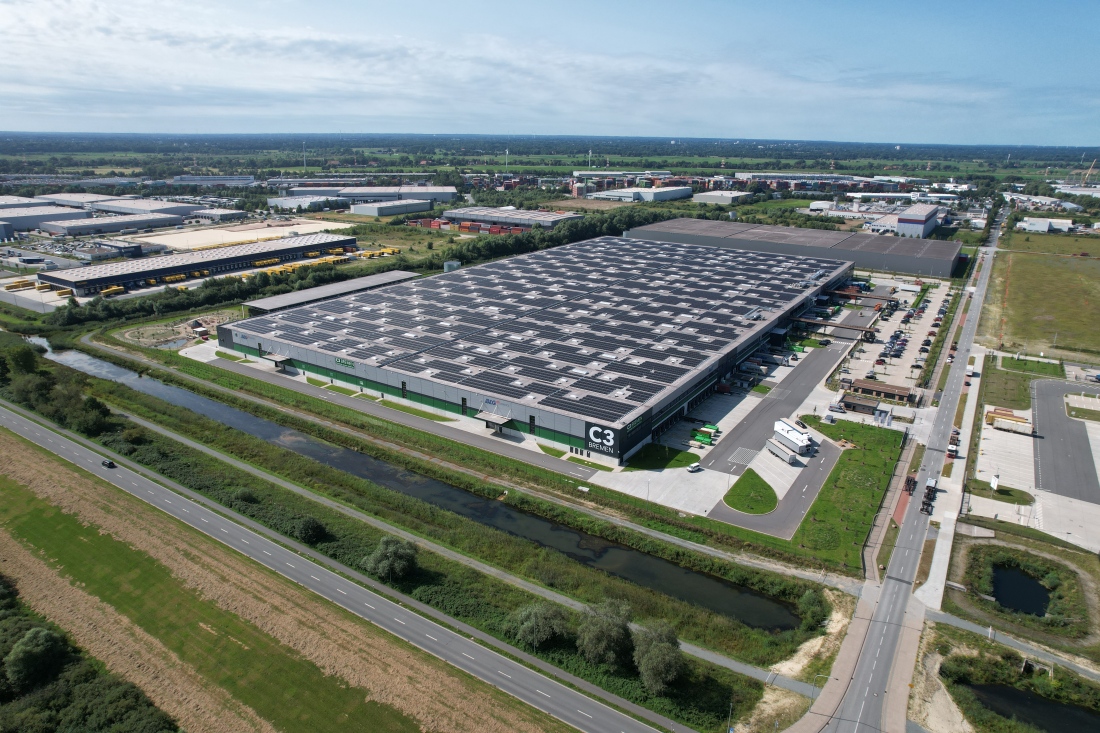 Eine große Logistikhalle mit der Aufschrift "C3 Bremen". Auf der Fläche davor stehen Lkw und Container.