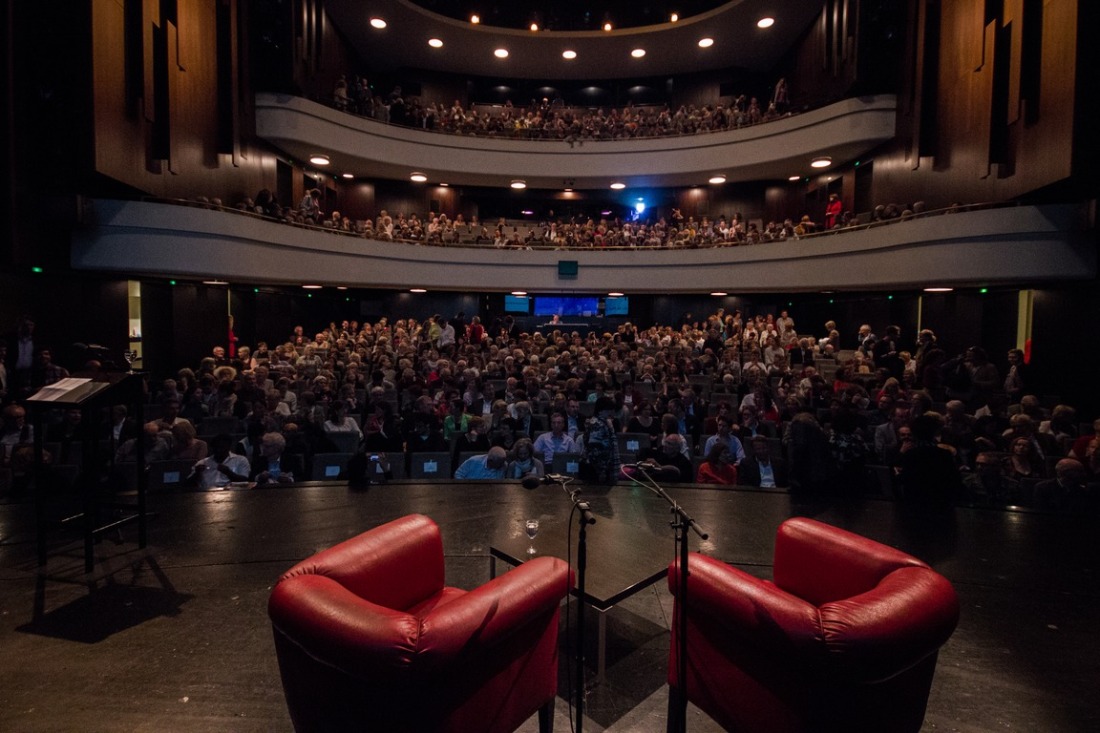 Blick von einer Bühne mit zwei roten Sesseln auf ein Publikum