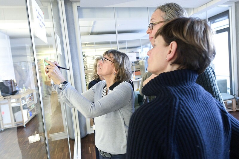 Bei einer Verantstaltung beschriften Personen Klebezettel an einer Glaswand. Bei einer Verantstaltung beschriften Personen Klebezettel an einer Glaswand.