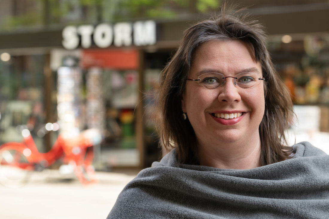 Eine Frau steht draußen. Im Hintergrund sieht man das Logo Storm Eine Frau steht draußen. Im Hintergrund sieht man das Logo Storm