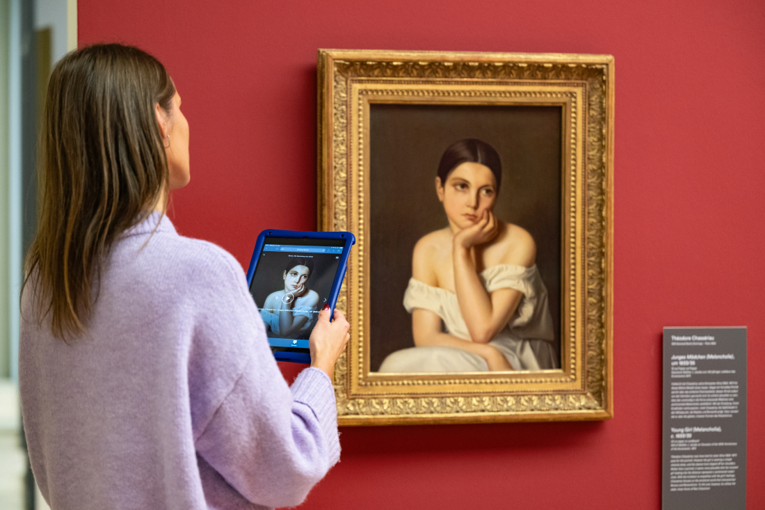 Eine Frau hält ein Tablet und sieht sich ein Gemälde an