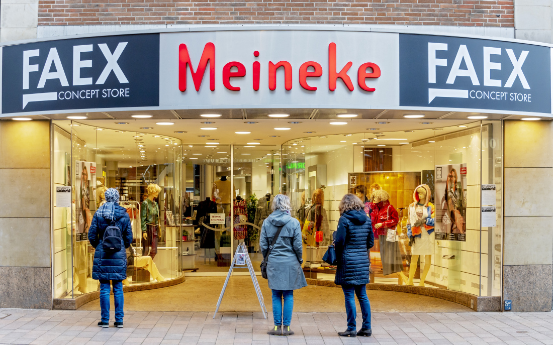 Die Außenansicht eines Einzelhandelsgeschäftes mit großen Fenstern, in denen Mode an Schaufensterpuppen zu sehen ist. Vor den Fenstern stehen drei Frauen.