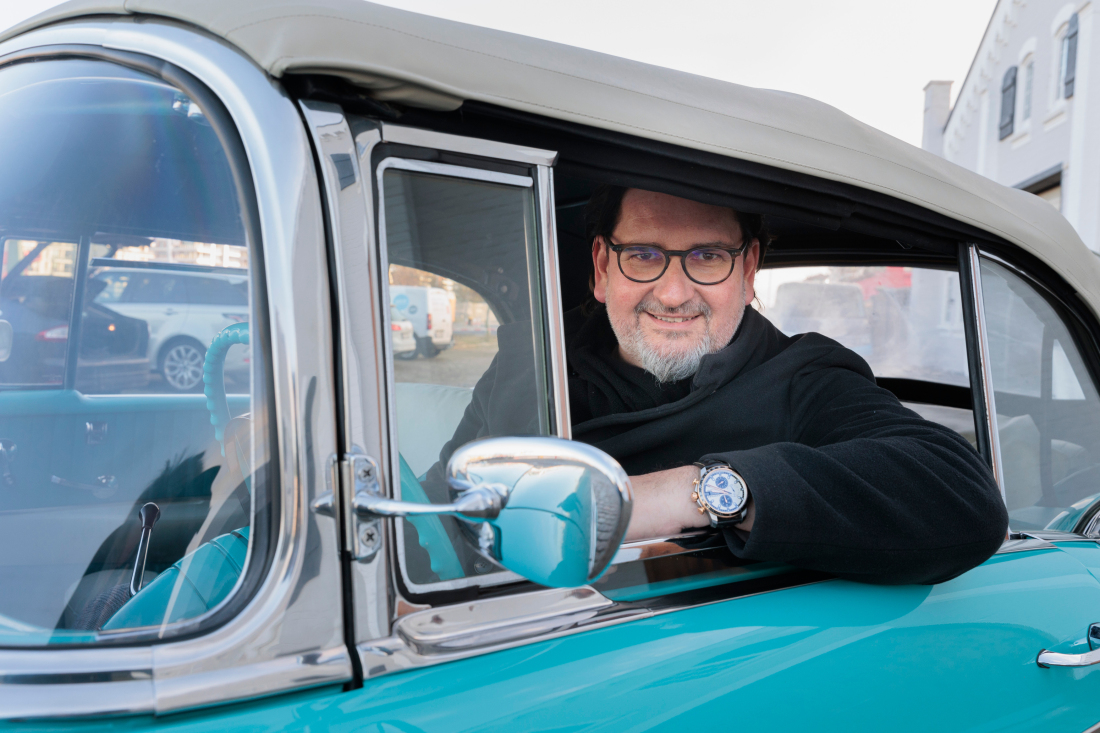 A man is sitting in a car and smiles into the camera