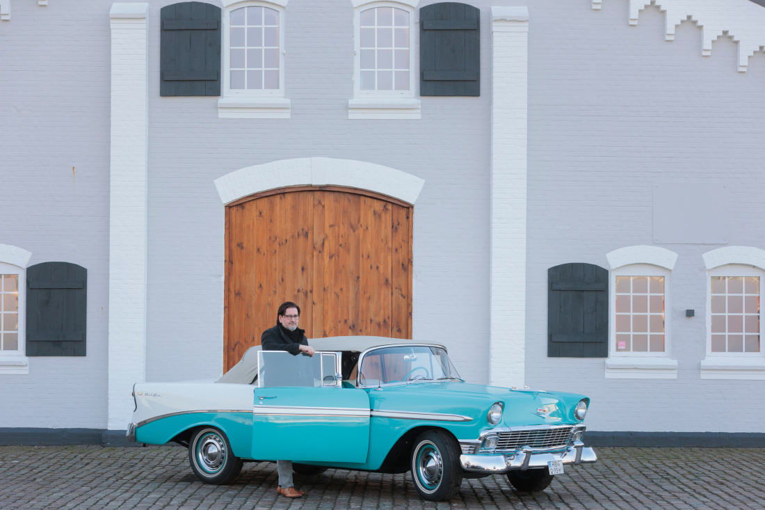 A man is standing in front of a blue chevrolet