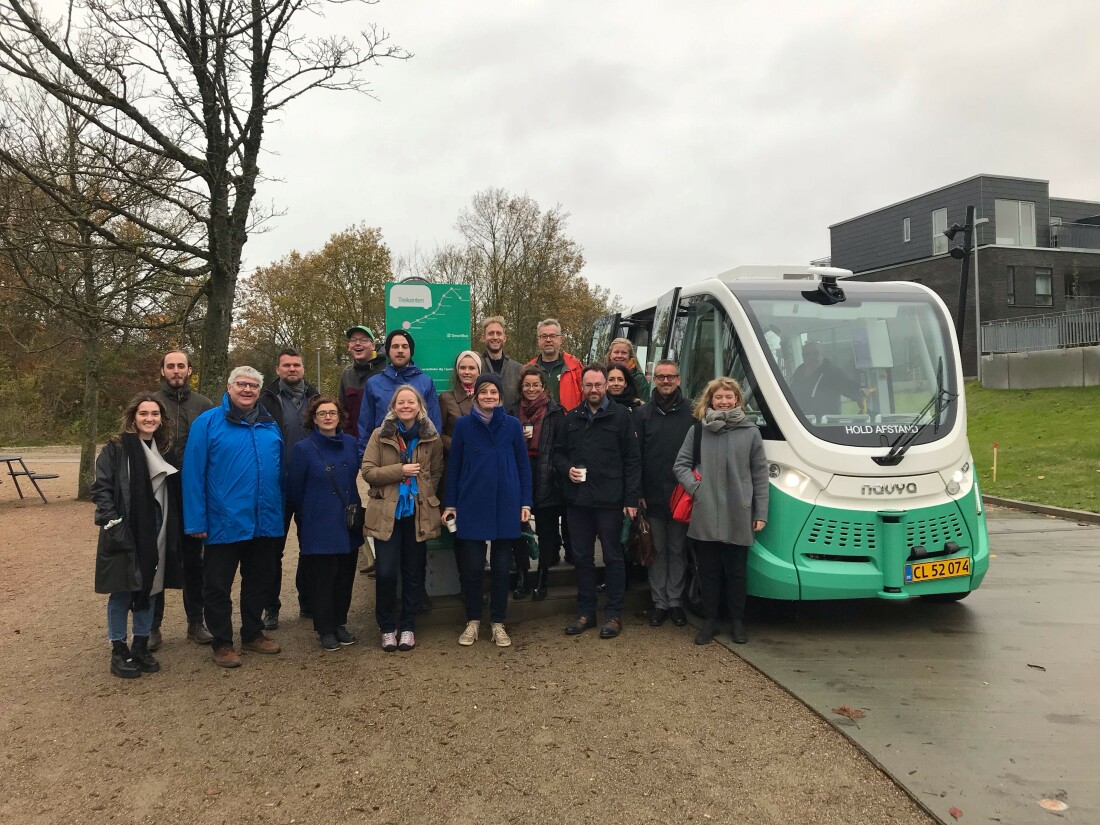 A group of people is standing in front of a small bus and smiles into the camera