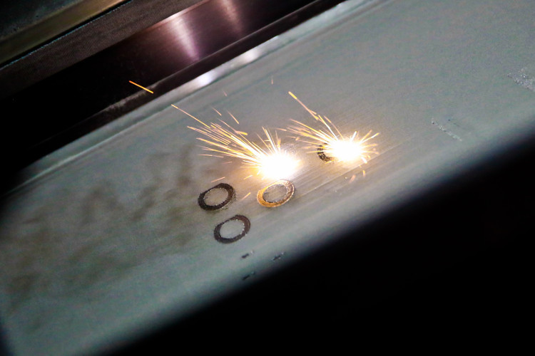 A laser makes sparks fly as it forms components layer by layer in the grey metal powder 