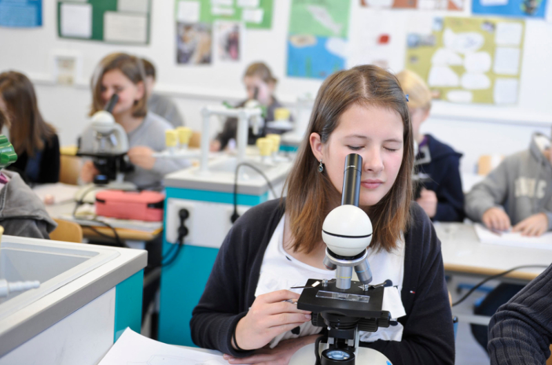 Junge Schülerin bei der Arbeit mit einem Mikroskop