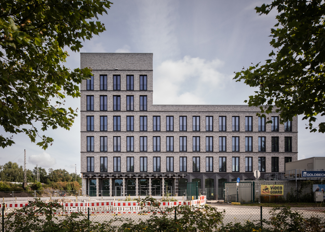 Ein großes Gebäude aus hellen Steinen, es hat die Form eines "liegenden" großen Ls. Der höhere Teil hat sechs Stockwerke, der andere vier.