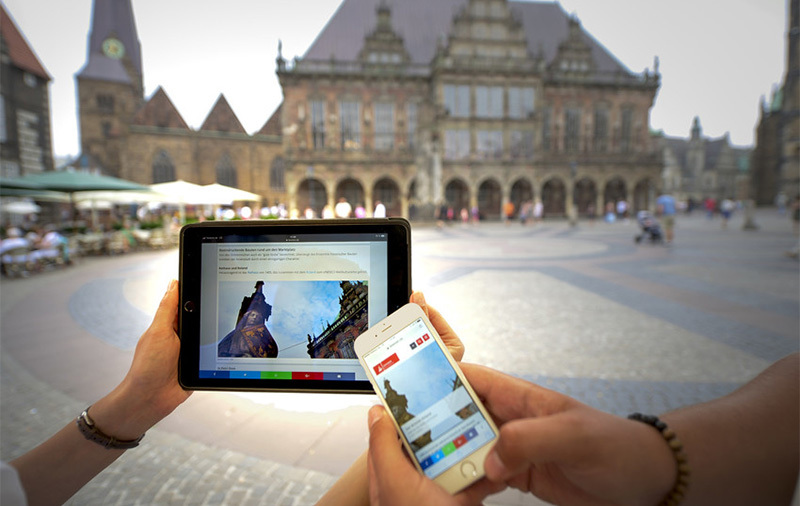 Man sieht die Hände von zwei Personen. Eine hält ein Smartphone, die andere ein Tablet.
