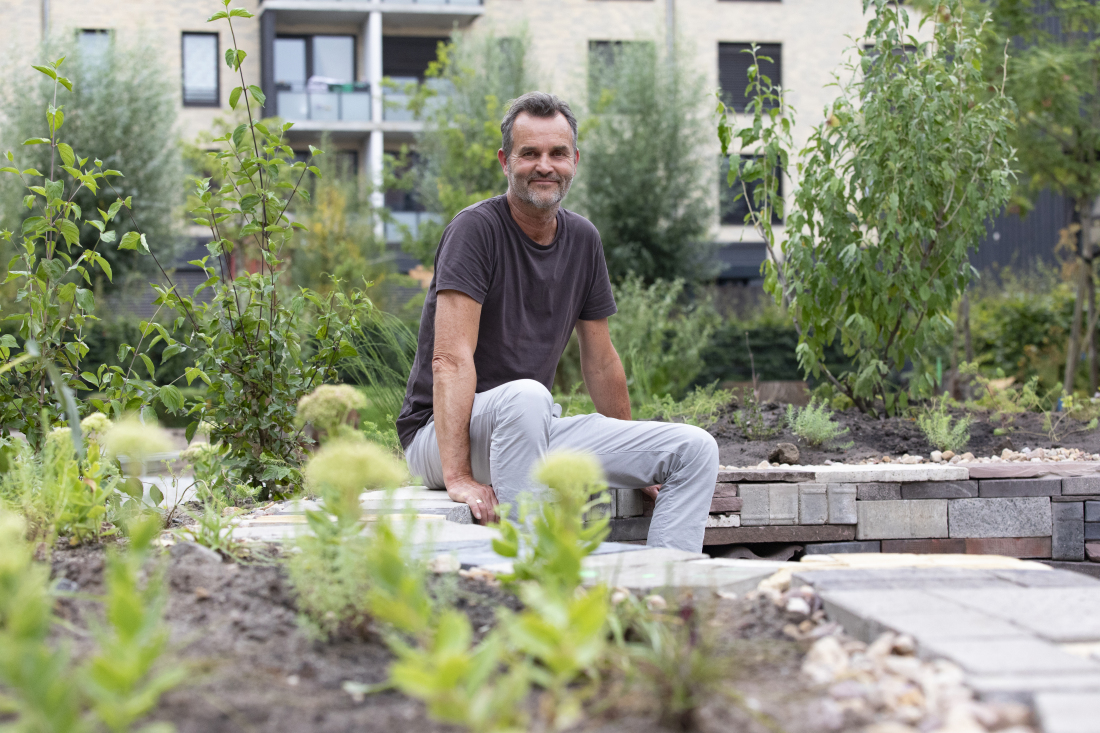 Volker Kranz sitzt auf einer niedrigen Steinmauer in einem Garten.