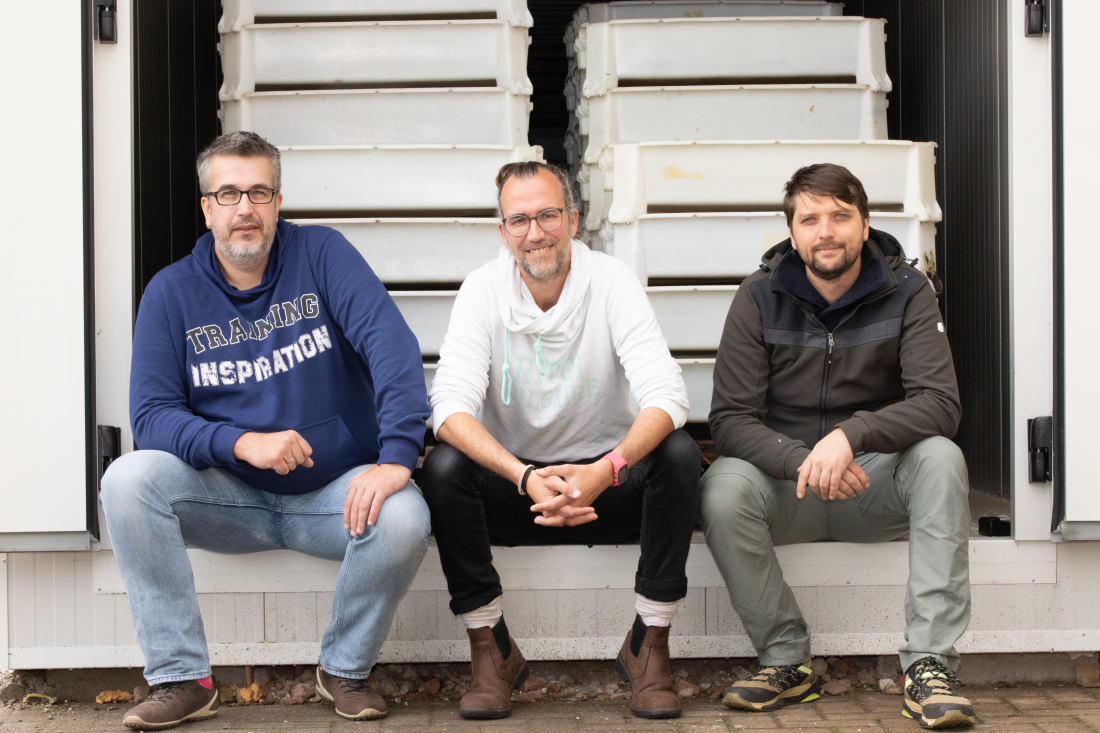 Amir Mehmedović, Norman Breitling and Florian Berendt (from left) sit at the entrance to the 70-meter-long container tube where the fly larvae are fed in boxes. 