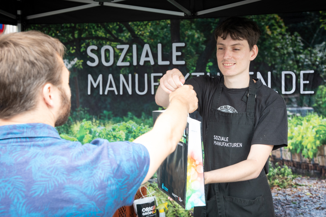 Josua Rückels (rechts) überreicht einem Kunden seinen Einkauf. Die Arbeit auf den Wochenmärkten und der stetige Austausch mit der Kundschaft soll die Teilnehmenden des Projekts bestärken. 