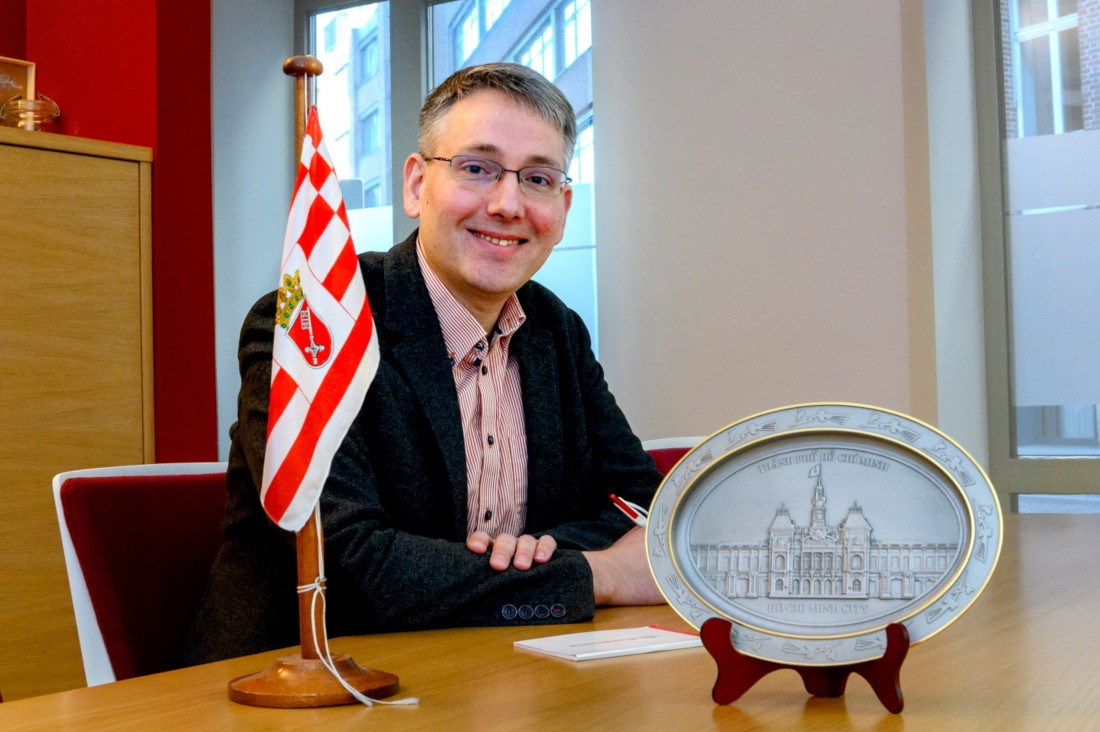 Bremeninvest project manager Manuel Kühn with the Bremen flag and a plate showing Ho Chi Minh City’s town hall. 
