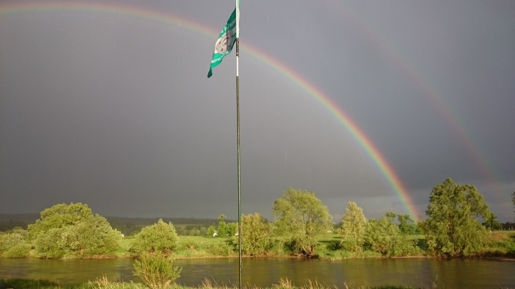Die Werderfahne vor der Weser mit Doppeltem Regenbogen im Hintergrund