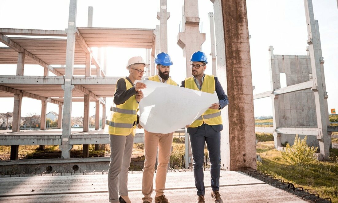 Drei Fachkräfte begutachten einen Plan auf einer Baustelle