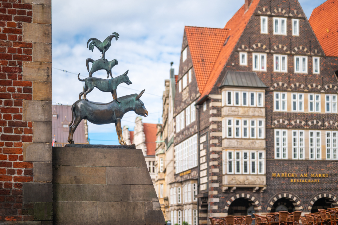 Bronzestatue der Bremer Stadtmusikanten: Ein Esel trägt einen Hund, darauf steht eine Katze, ganz oben ein Hahn. Die Figur steht an einer Sandsteinmauer vor historischen Häusern in der Bremer Altstadt. Bronzestatue der Bremer Stadtmusikanten: Ein Esel trägt einen Hund, darauf steht eine Katze, ganz oben ein Hahn. Die Figur steht an einer Sandsteinmauer vor historischen Häusern in der Bremer Altstadt.
