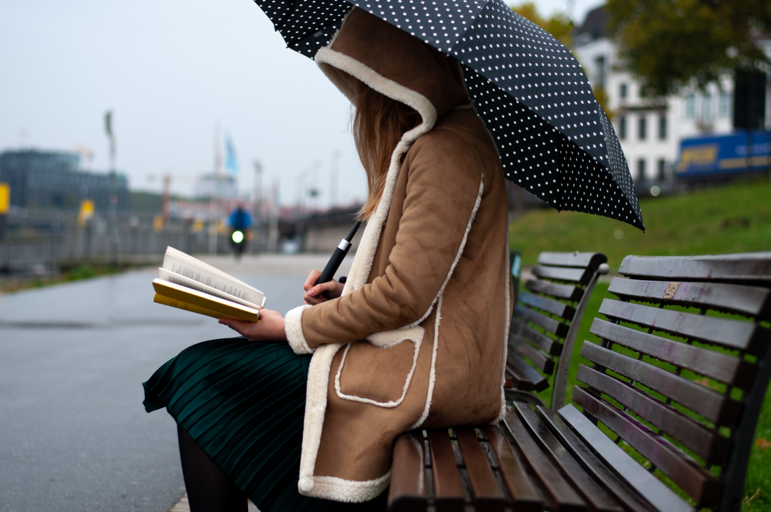 Eine Frau sitzt auf einer Bank mit einem Regenschirm und liest ein Buch