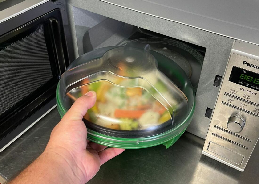 Eine Hand legt ein Gericht in die Mikrowelle